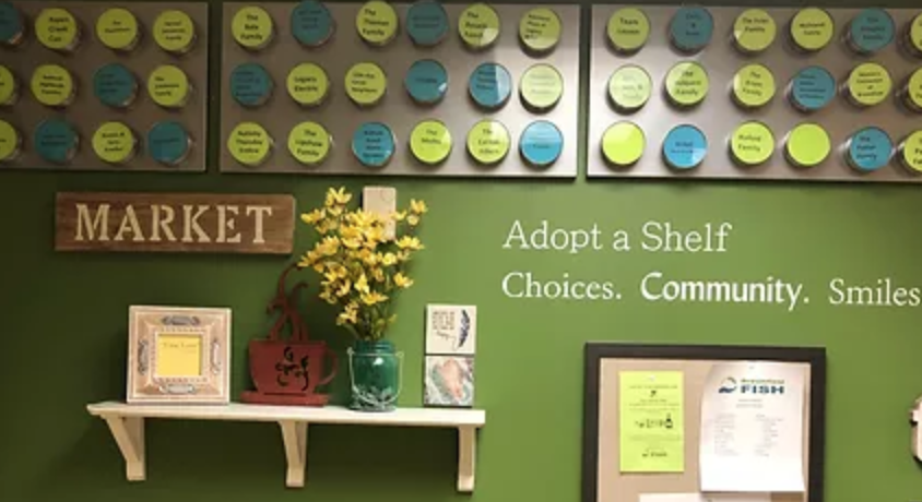 The Adopt A Shelf wall in the Broomfield FISH Marketplace, featuring metal boards with magnets listing the names of Adopt A Shelf donors.