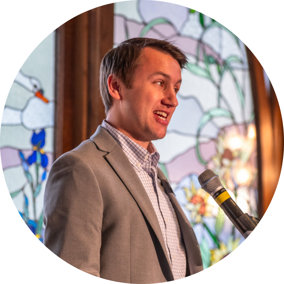 A speaker at Broomfield FISH's Embracing Hope Luncheon standing in front of a microphone in front of a stained glass window.